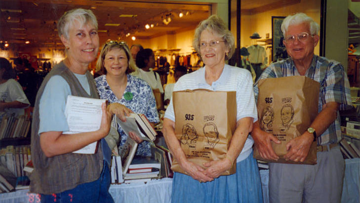 A photograph of the library booksale at Washington Square Mall. Pictured are Sandy Schultheis, Lezlie Simmons, Millie Clifford, and Sam Clifford.