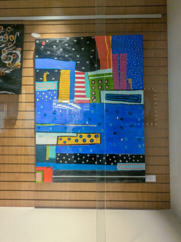 Colorful abstract painting depicting a cityscape with various geometric shapes representing buildings against a night sky filled with stars. The artwork features bold blocks of blue, green, red, yellow, and black, with patterns of dots and lines adding texture and depth.